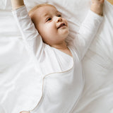 Weißer Babybody mit karamellbraunem Häkel-Detail aus Bio-Baumwolle – getragen von einem Baby