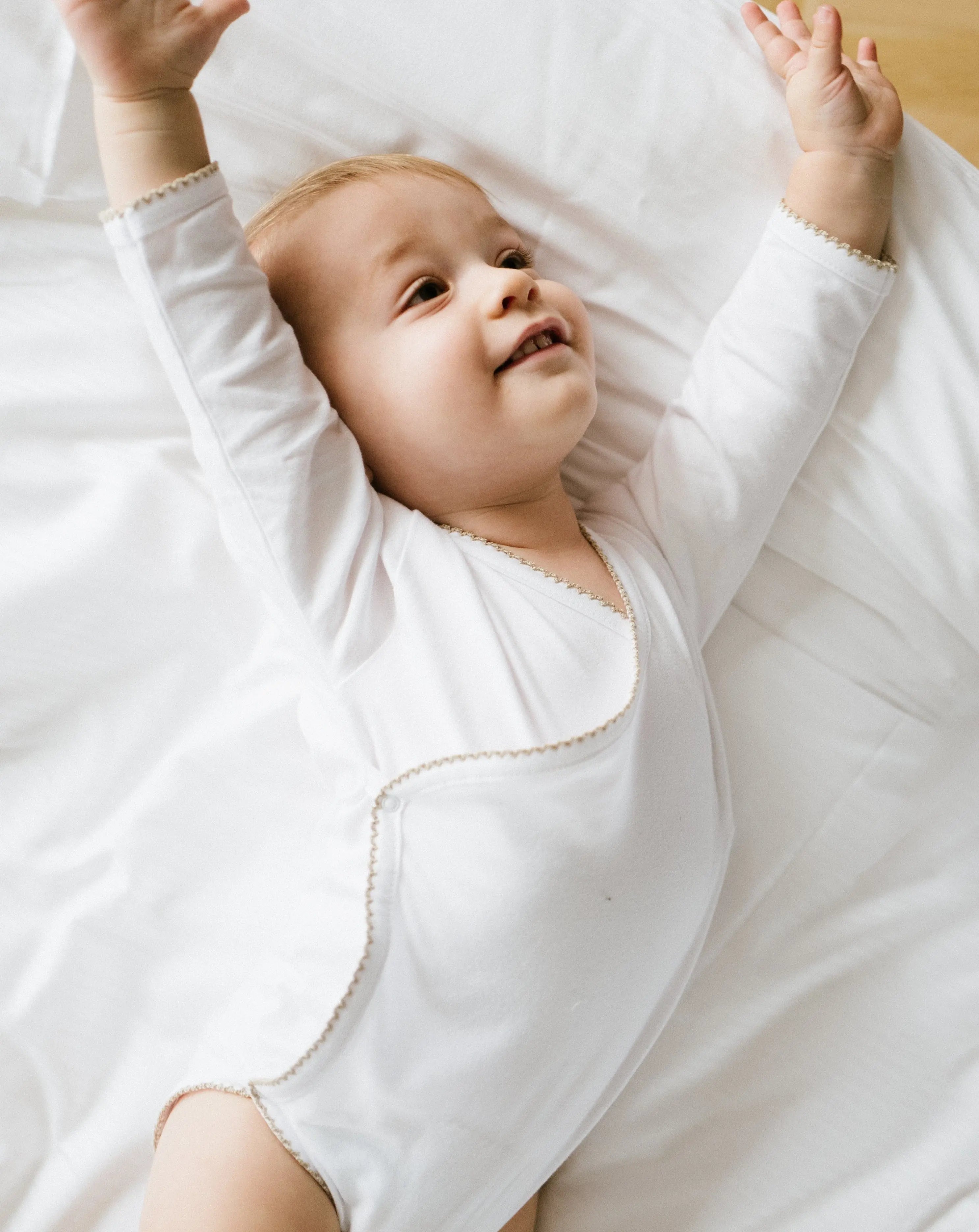 Weißer Babybody mit karamellbraunem Häkel-Detail aus Bio-Baumwolle – getragen von einem Baby