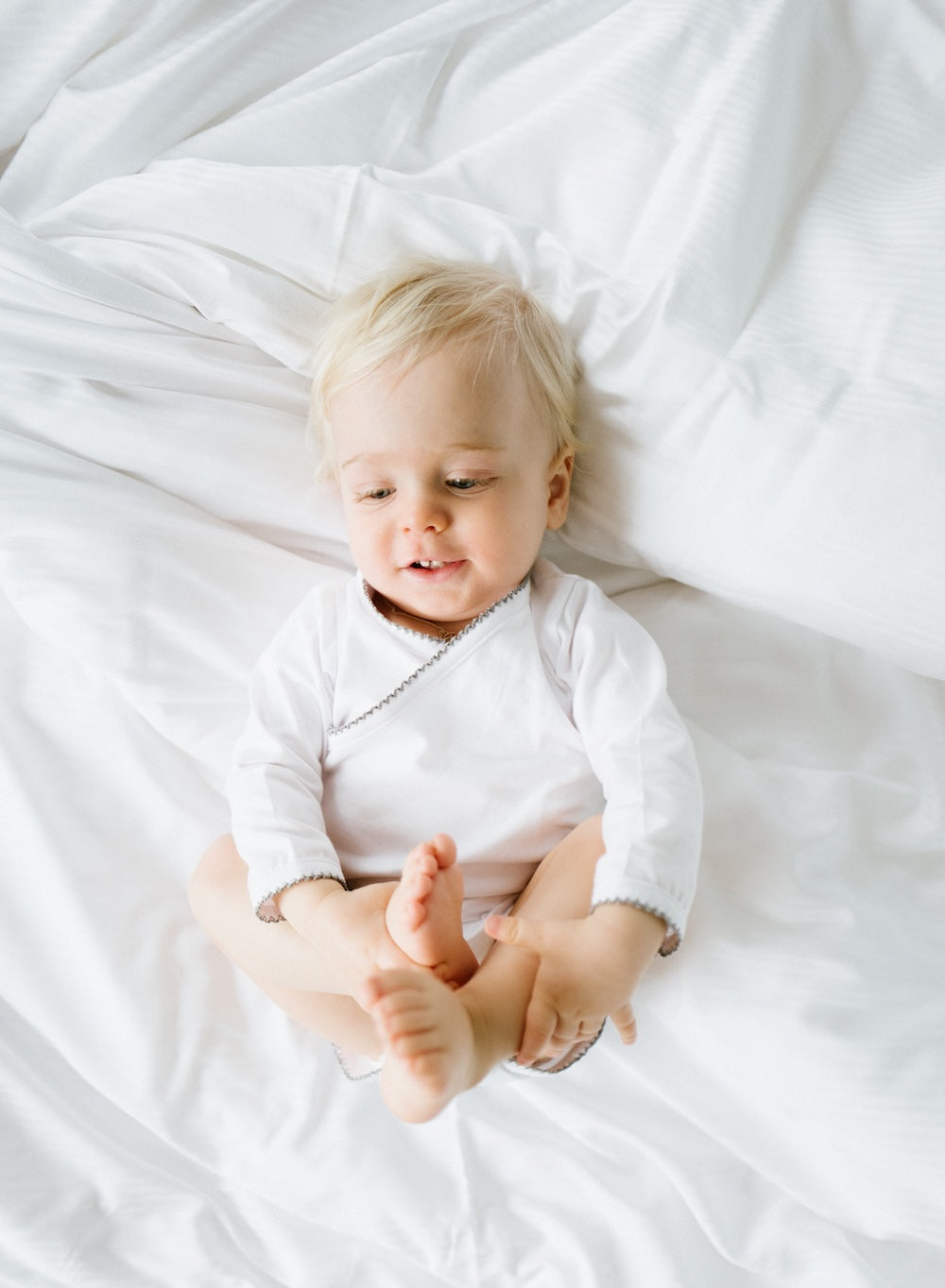 Baby lying on white bedding wearing soft organic cotton clothing 