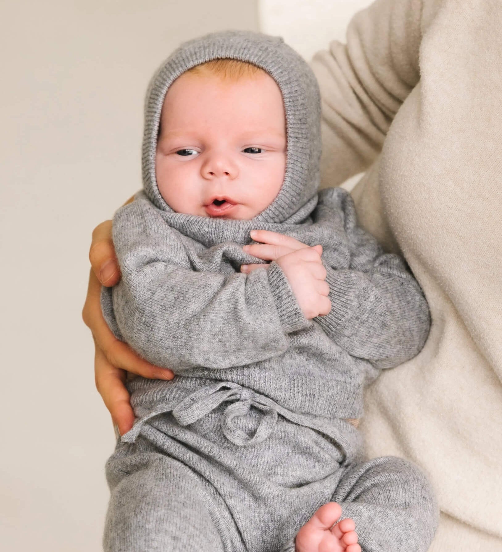 Baby wearing soft heather grey cashmere balaclava, warm knitted hood for infants.