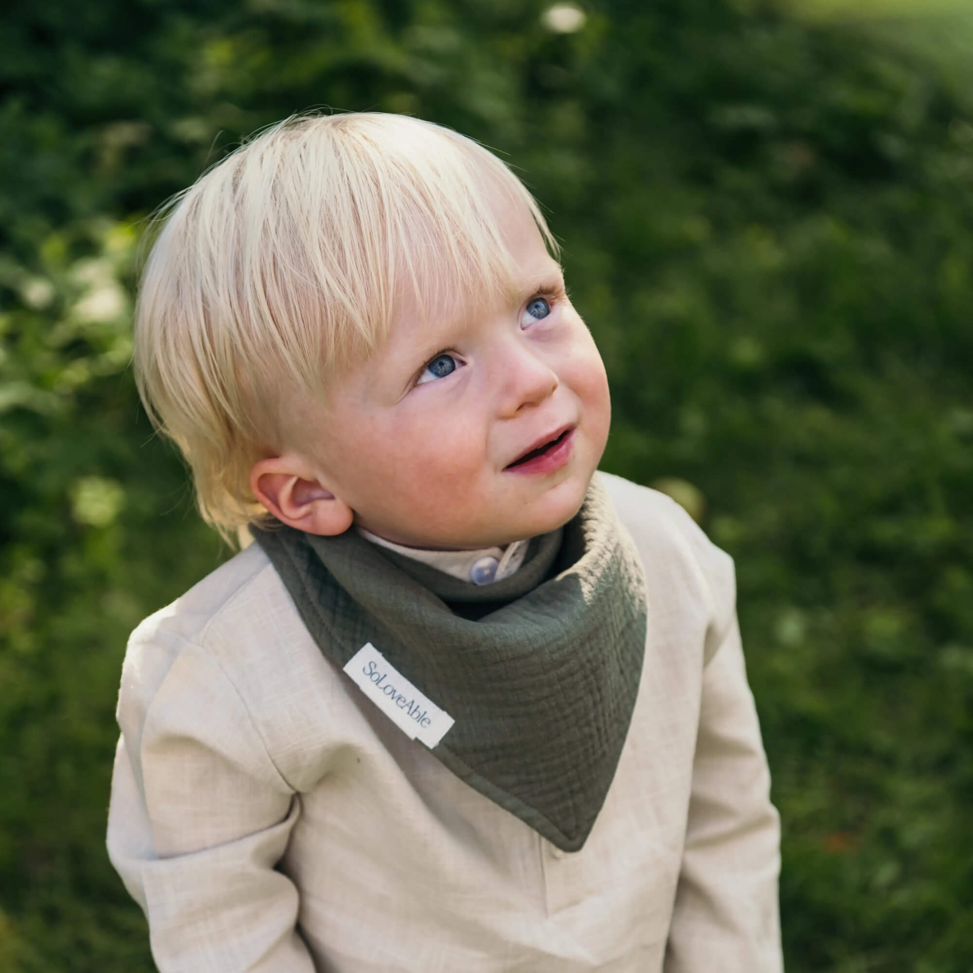 Soloveable baby wearing a green muslin bandana bib outdoors.