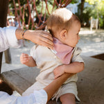 Soloveable baby wearing a pink muslin bandana bib during outdoor play.