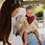 Soloveable baby wearing a red muslin bandana bib while playing outdoors.