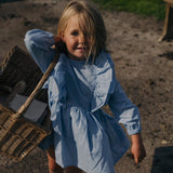 Child wearing blue linen ruffle dress outdoors, long sleeves, playful elegant kids clothing for everyday and special occasions