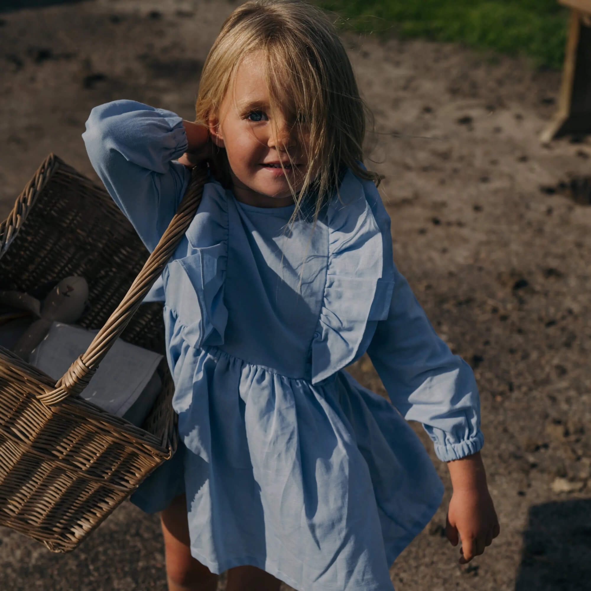 Child wearing blue linen ruffle dress outdoors, long sleeves, playful elegant kids clothing for everyday and special occasions