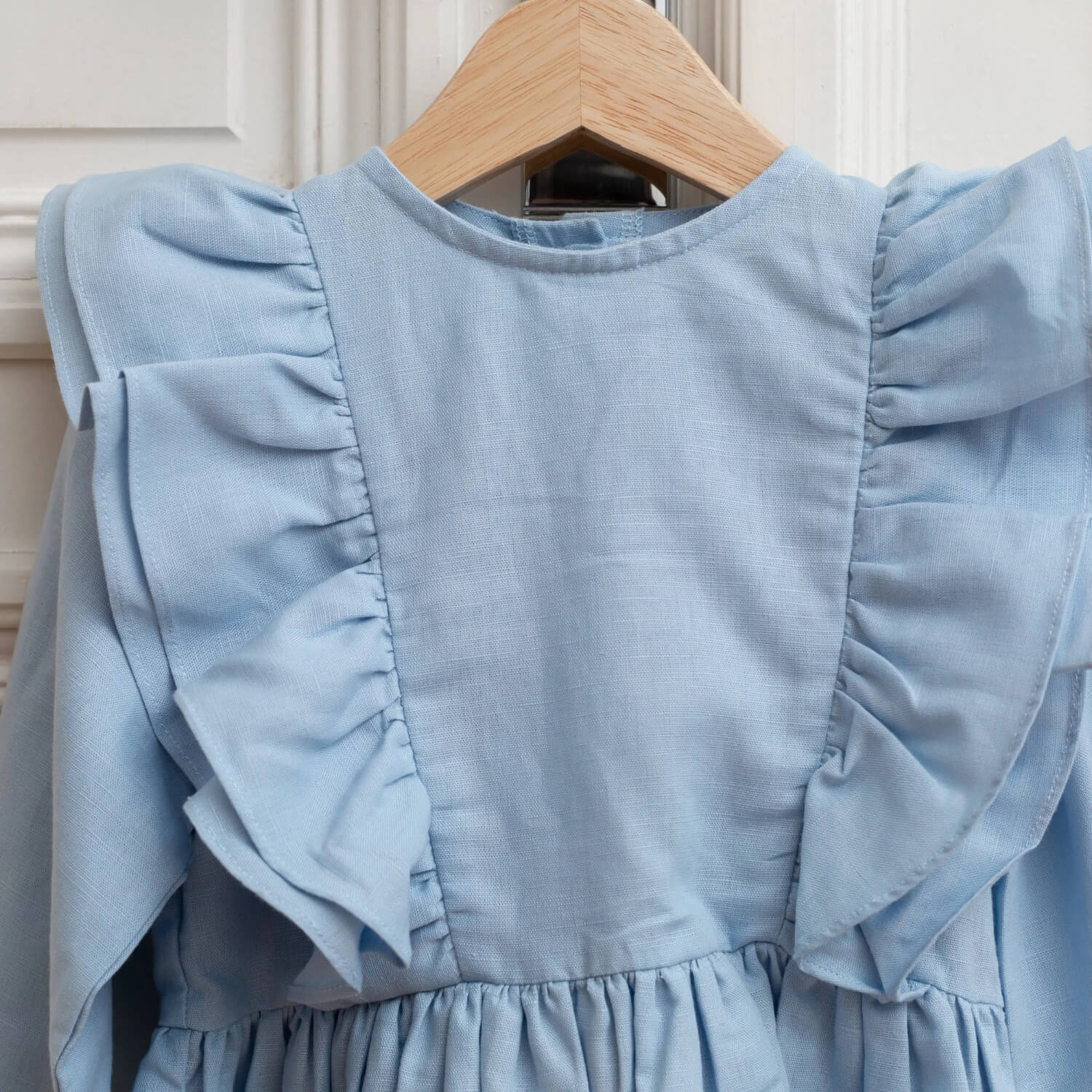 Close-up of blue linen girls dress with ruffle shoulder details.
