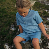 Toddler sitting outside wearing a blue linen short-sleeve shirt and matching shorts.