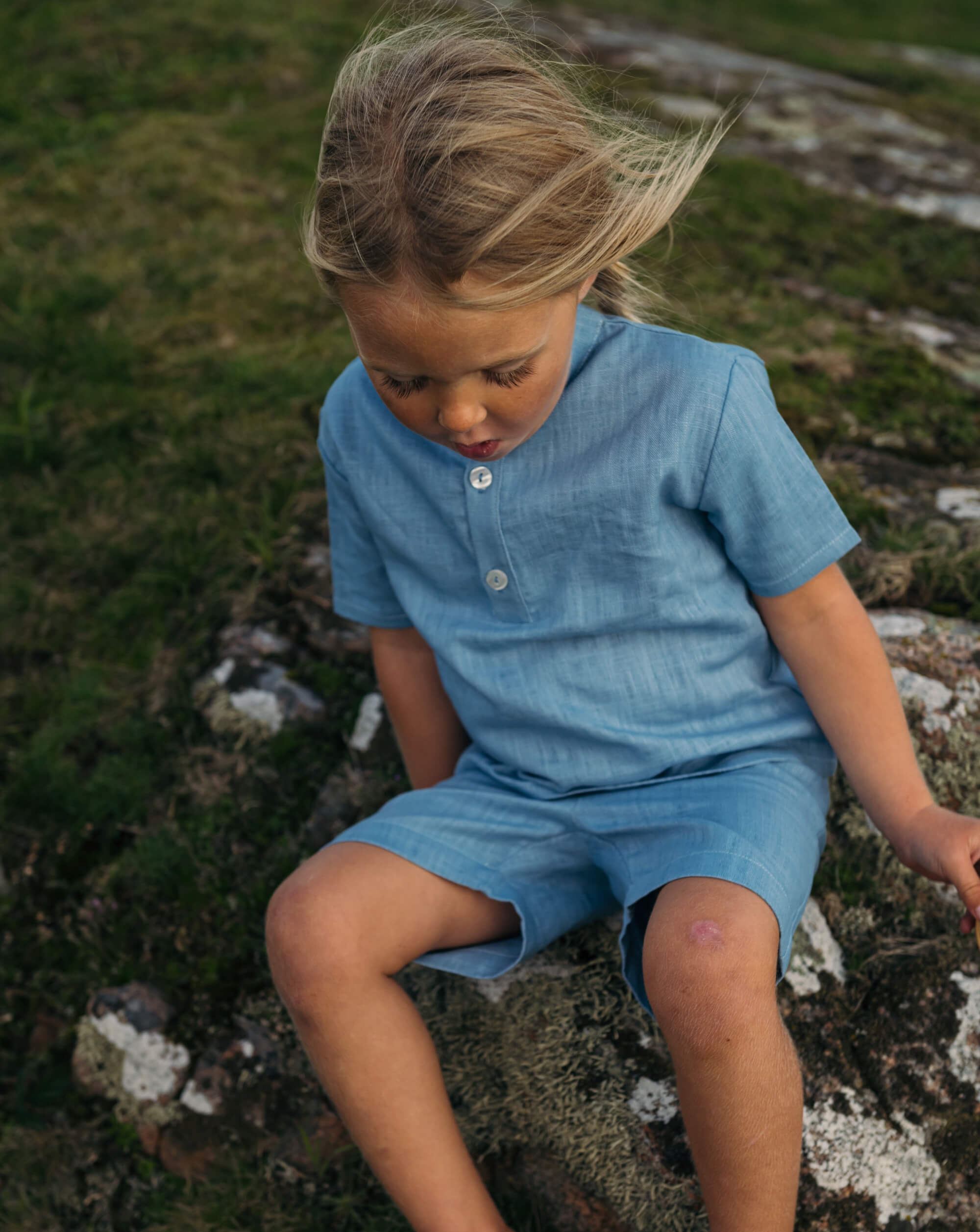 Toddler sitting outside wearing a blue linen short-sleeve shirt and matching shorts.