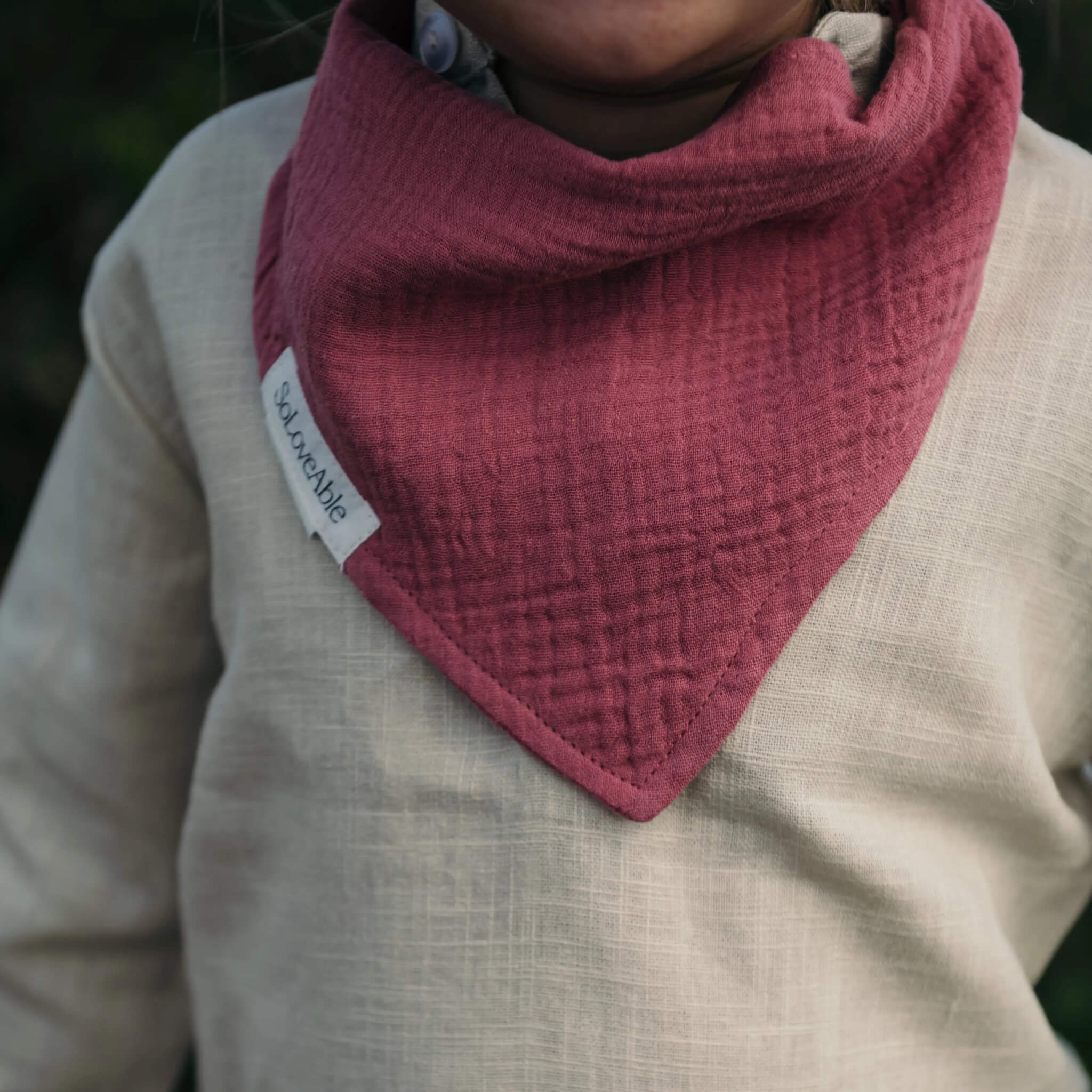 Soloveable close-up of a burgundy-colored muslin bandana bib worn by a baby.