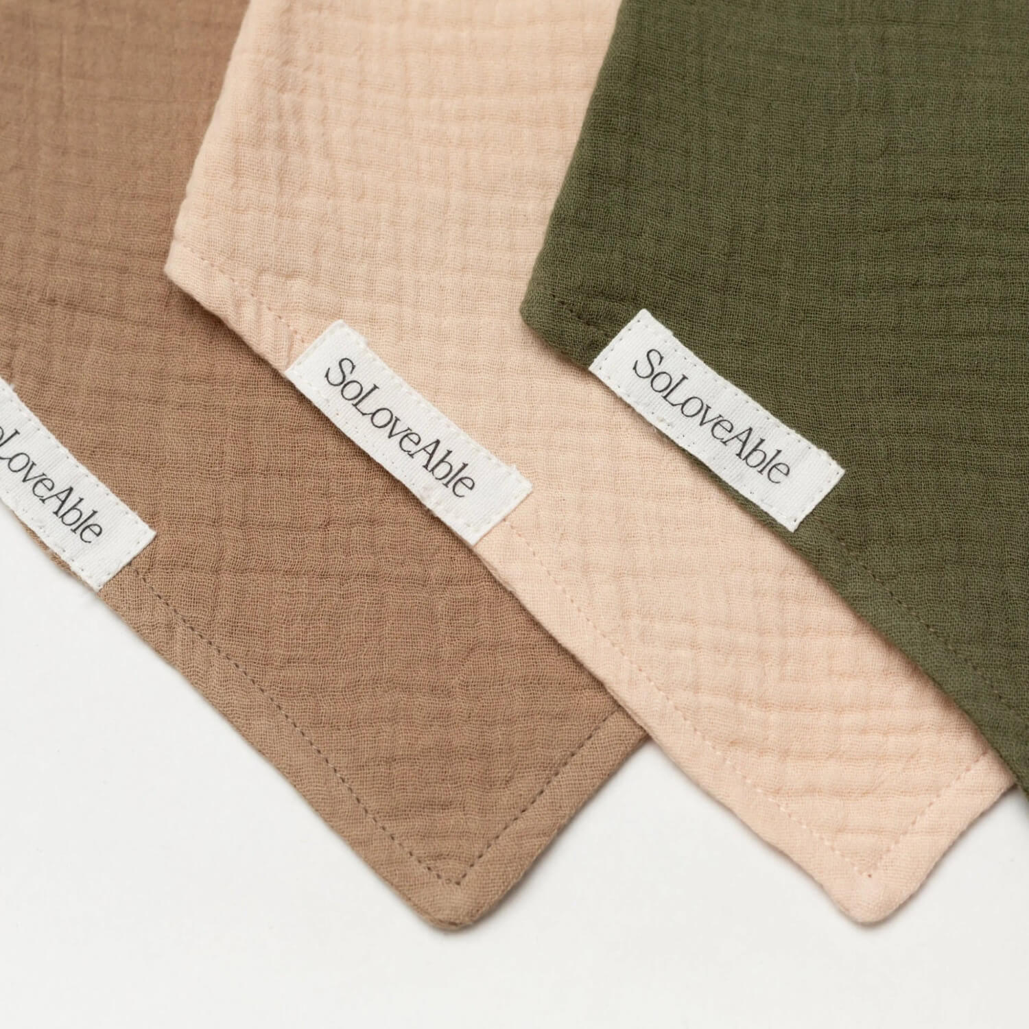 Close-up of Soloveable muslin baby bandana bibs in brown, beige and green.