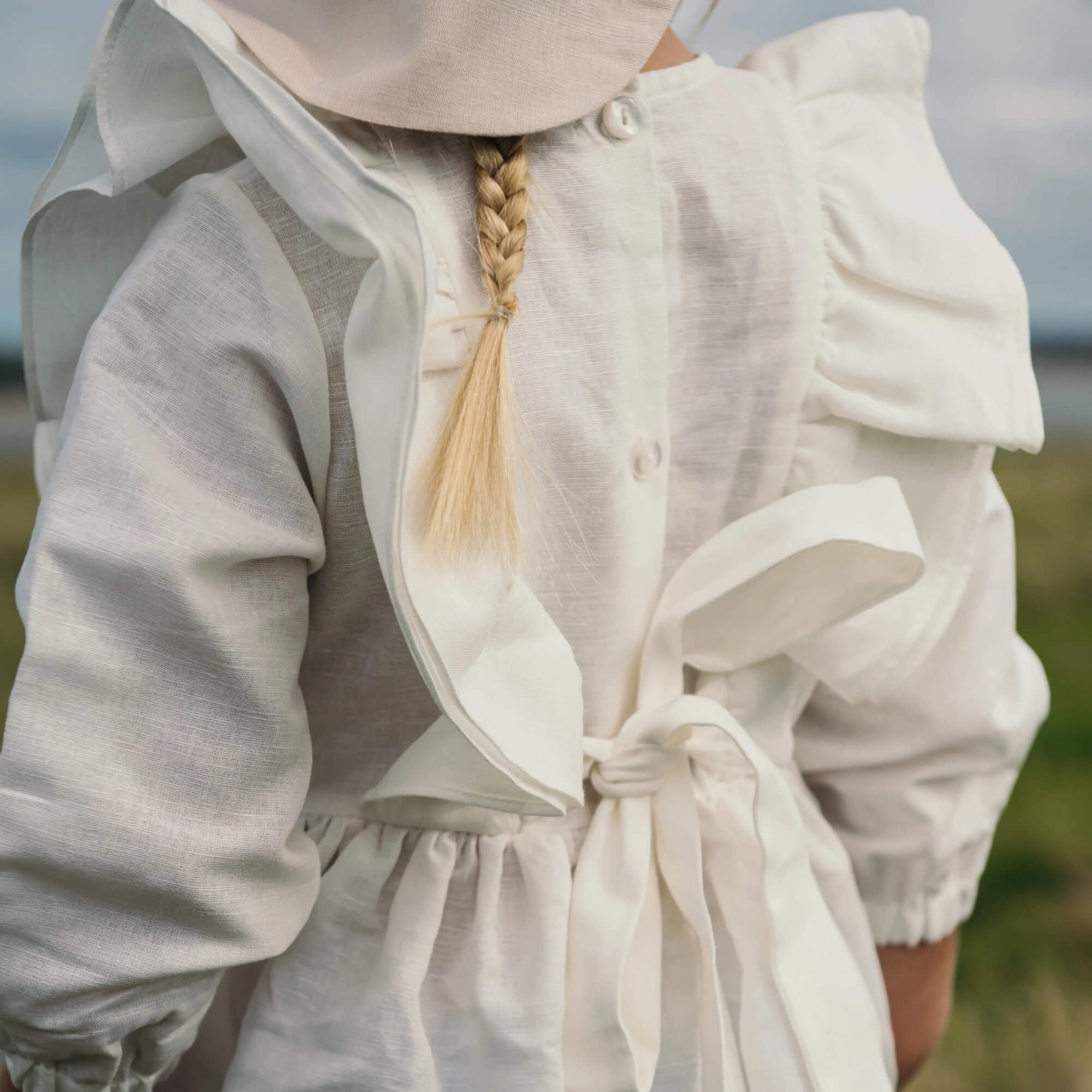 Child wearing a white linen dress with ruffle straps and tie-back detail outdoors