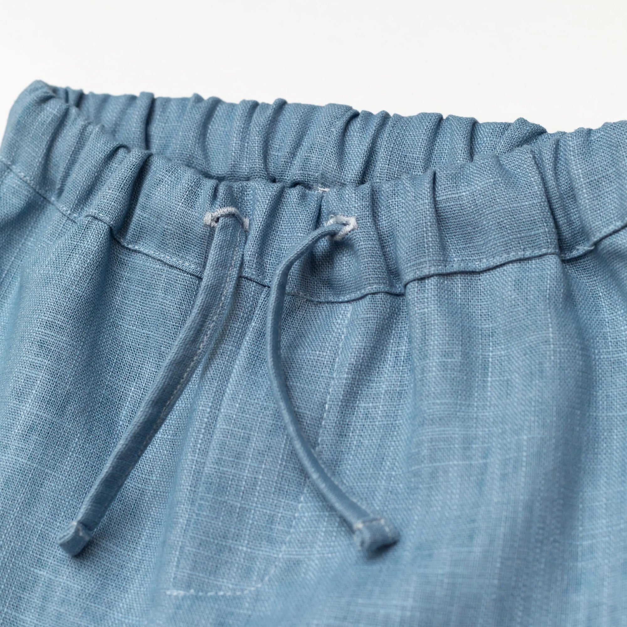 Close-up of the elastic waistband and drawstring on blue linen baby and toddler pants.