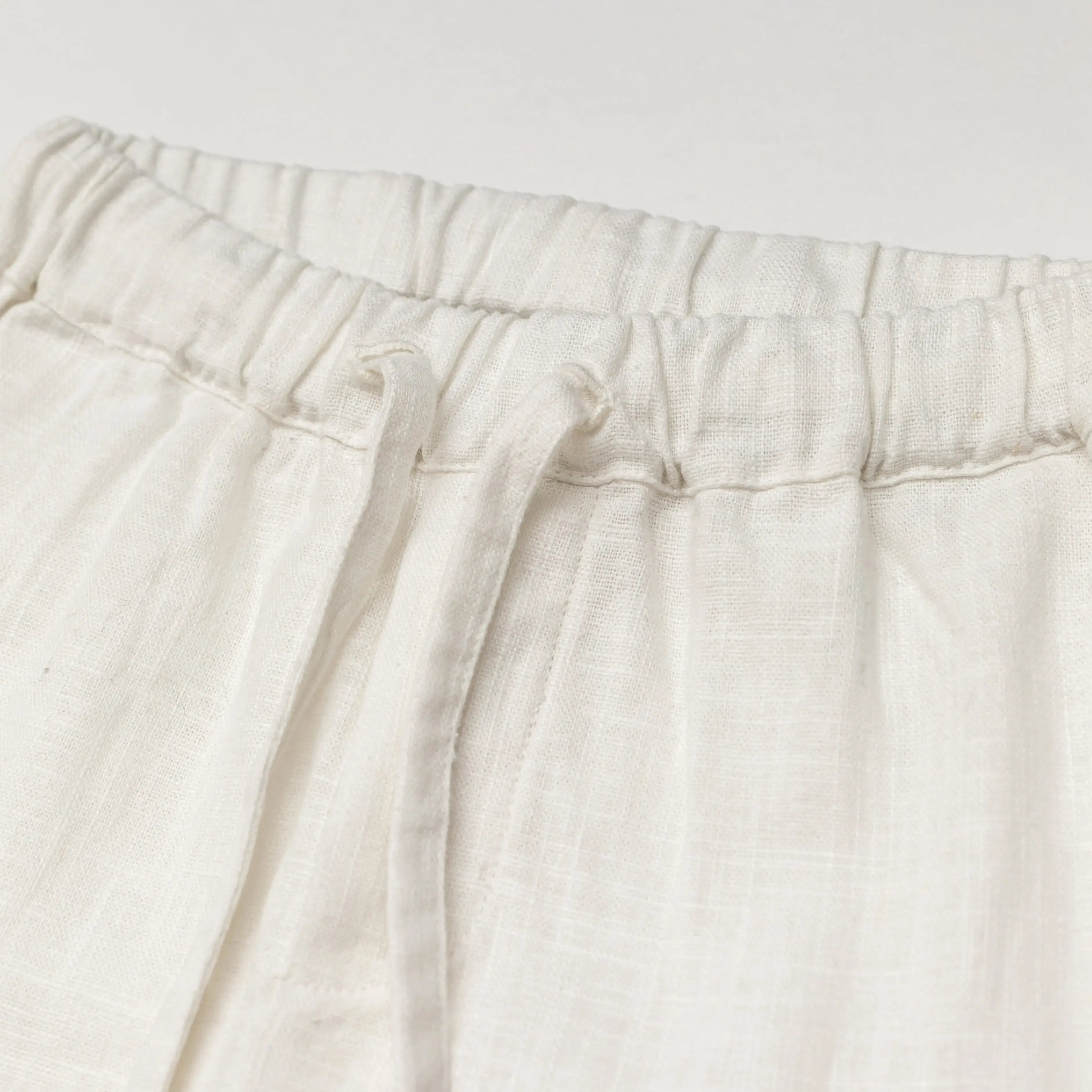 Close-up of the elastic waistband and drawstring on white linen baby and toddler pants.