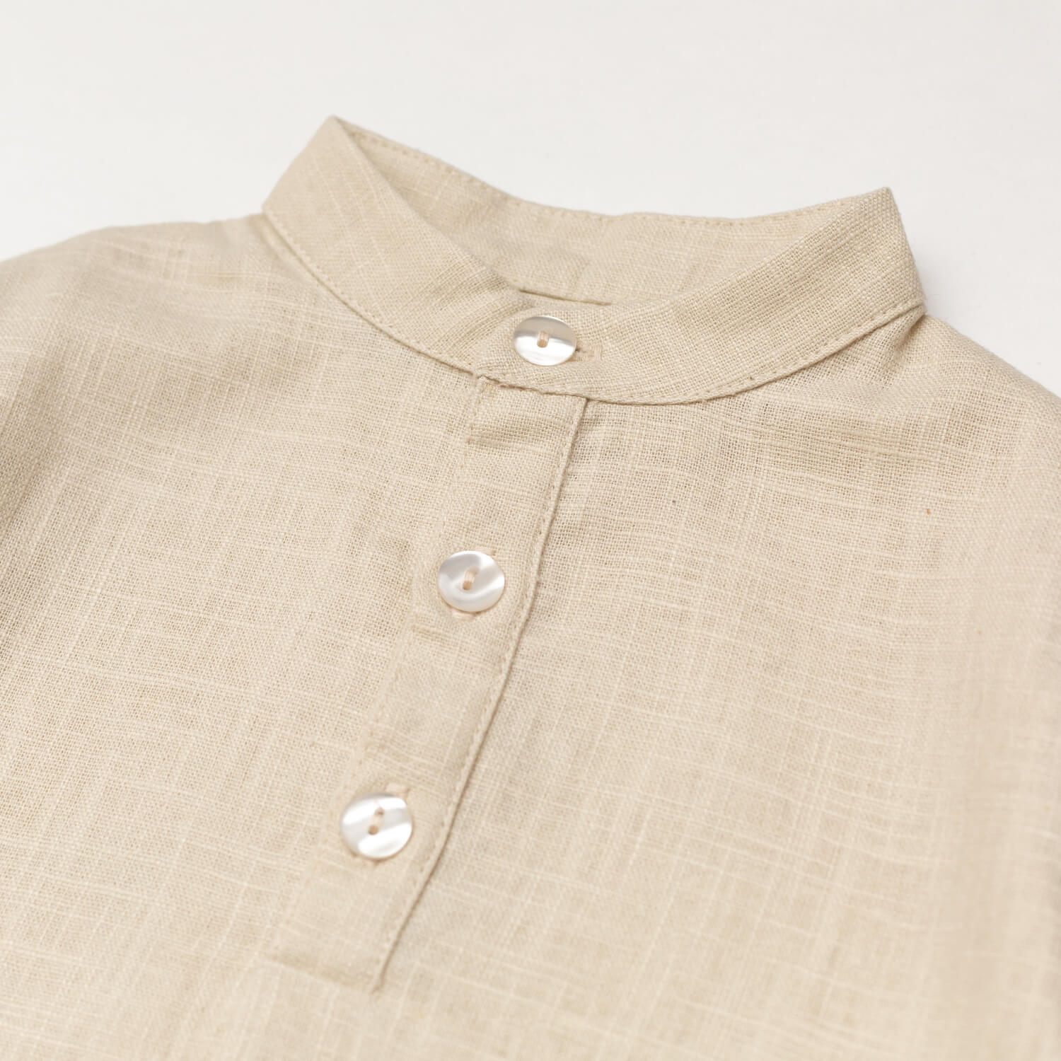 Close-up of the collarless neckline and button placket on the beige linen baby and toddler long-sleeve shirt.
