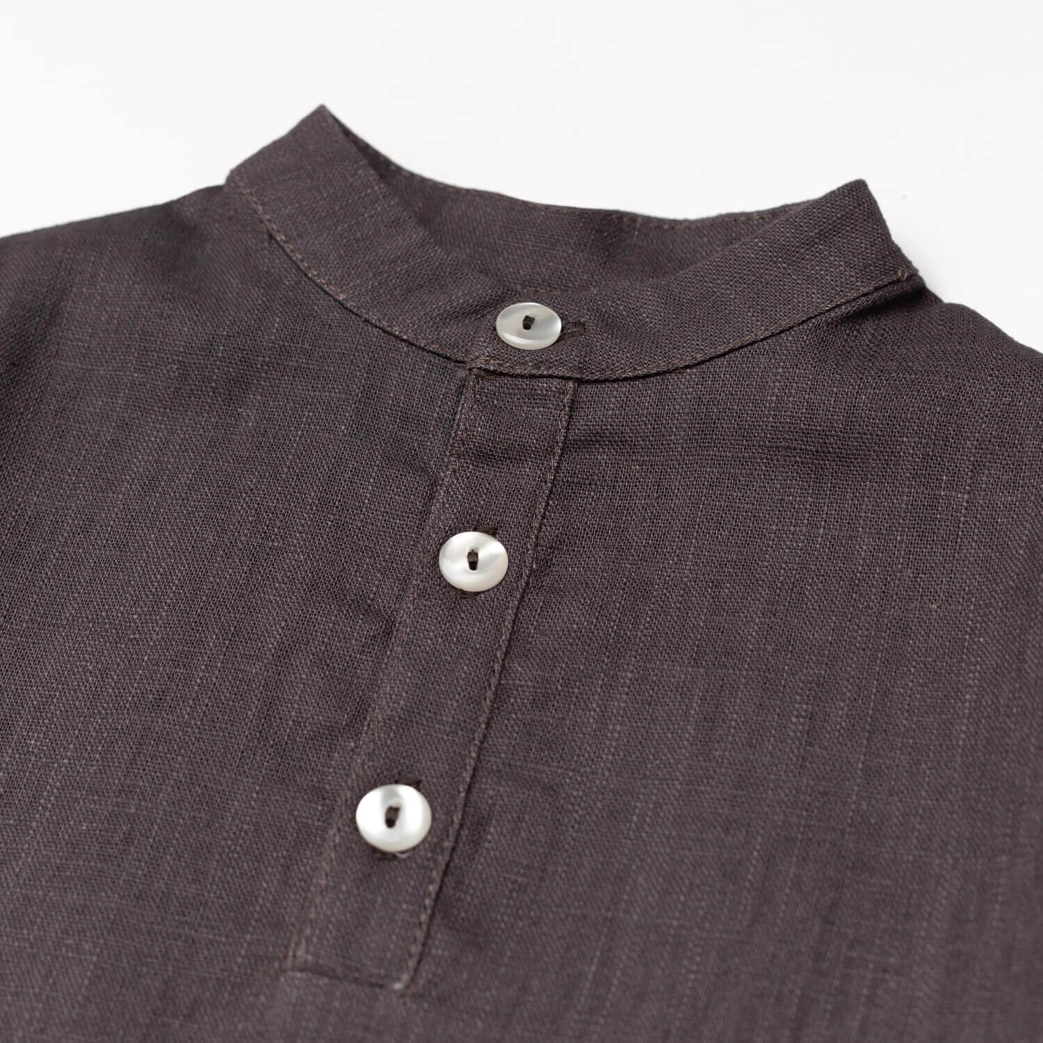 Close-up of the collarless neckline and button placket on the brown linen baby and toddler long-sleeve shirt.