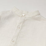Close-up of the collarless neckline and button placket on the white linen baby and toddler long-sleeve shirt.