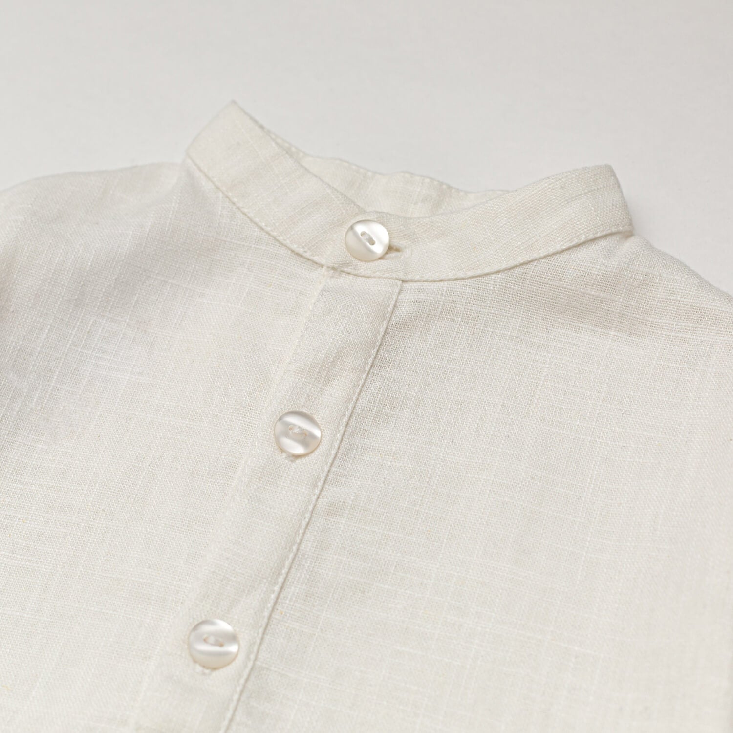 Close-up of the collarless neckline and button placket on the white linen baby and toddler long-sleeve shirt.