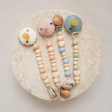 Pacifier clips made from silicone and natural wood beads in mixed pastel colors.