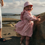 Smiling child wearing pink linen ruffle dress outdoors near the seaside, long sleeves, summer outfit by SoLoveAble