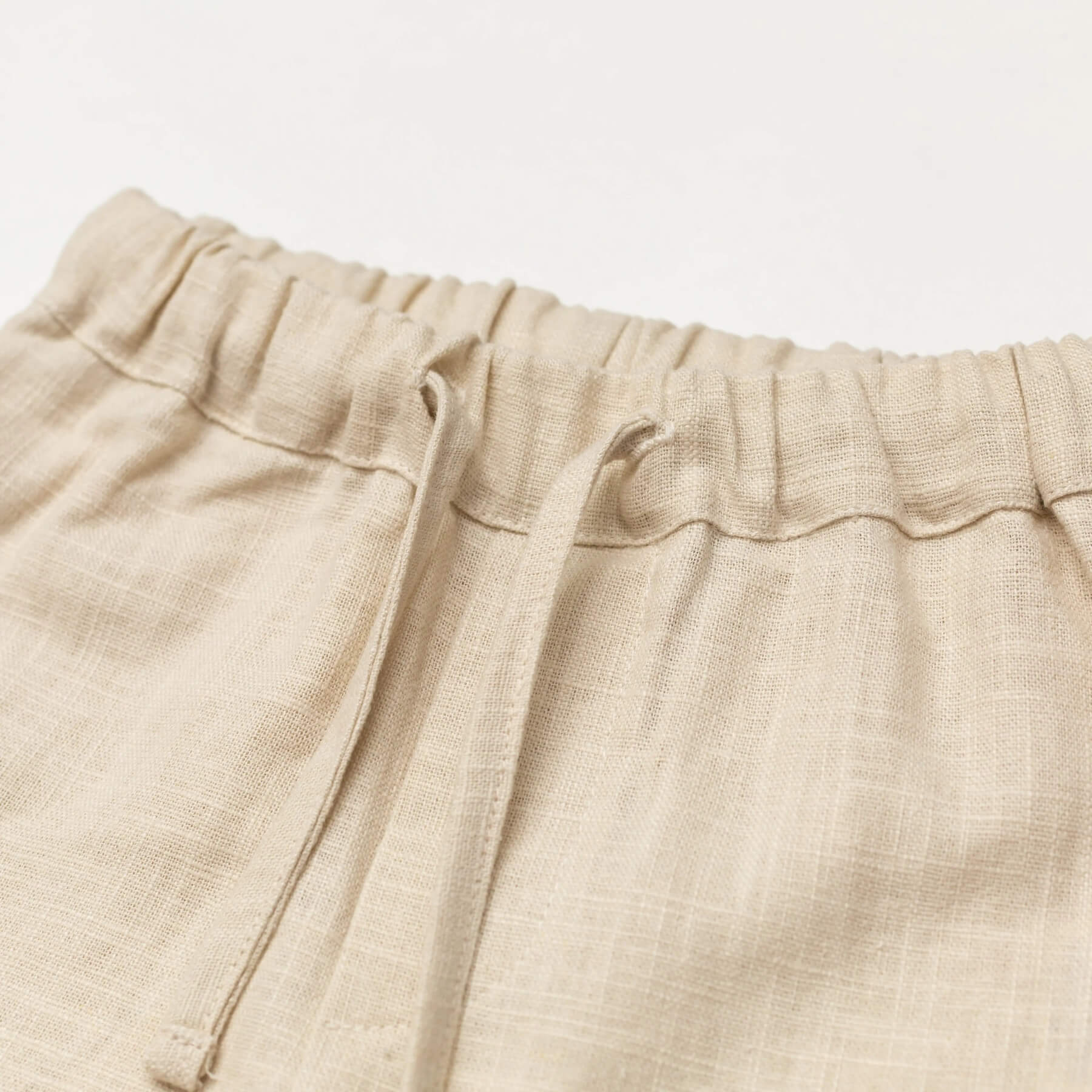 Close-up of the elastic waistband and drawstring on short beige linen pants for babies and toddlers.