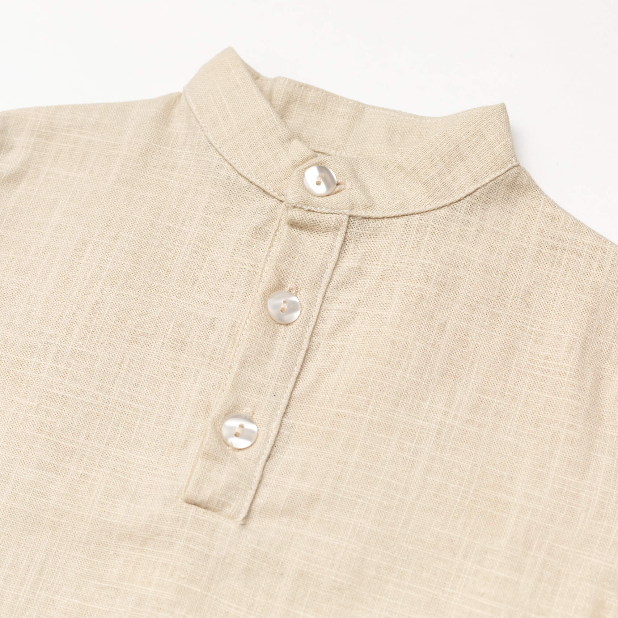Close-up of the collar and buttons on a beige linen short-sleeve shirt for babies and toddlers.