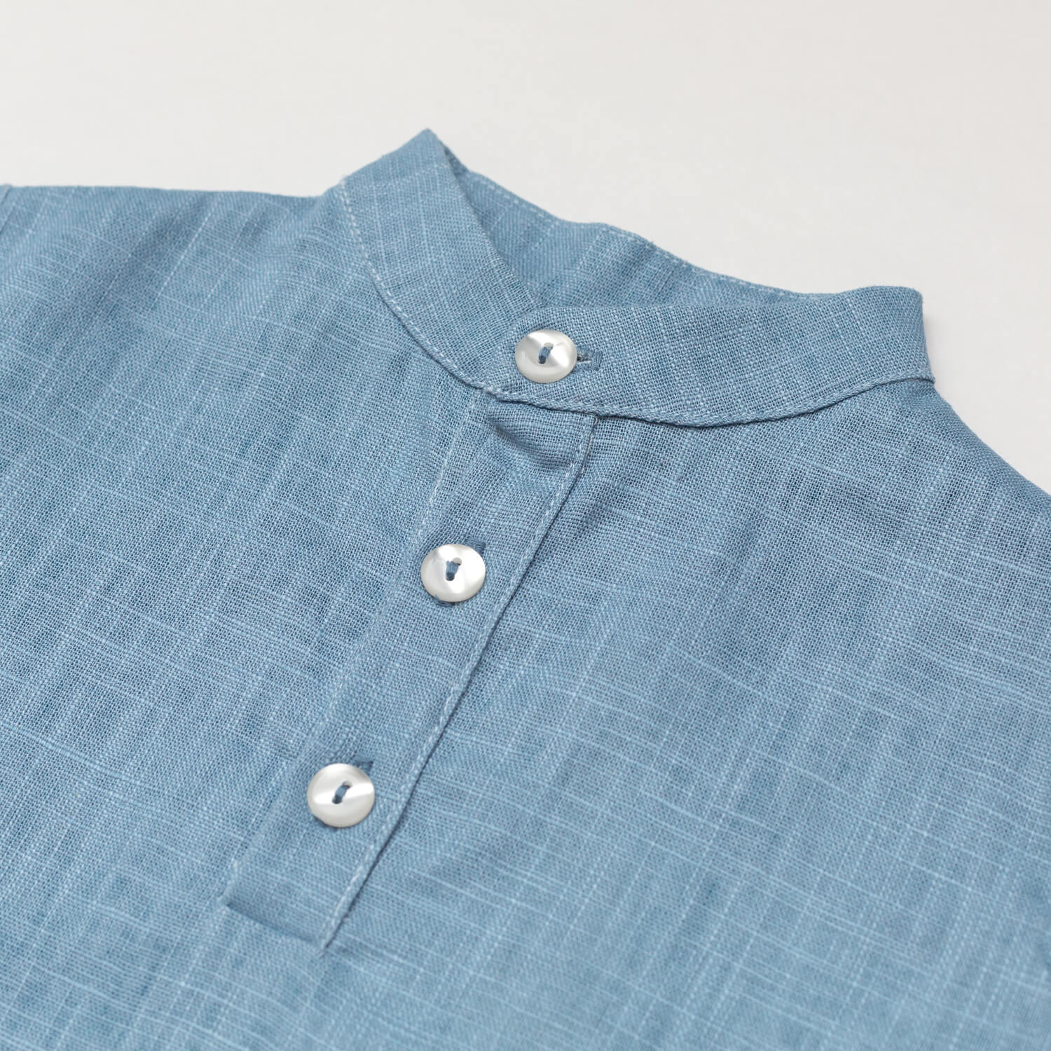 Close-up of the collar and buttons on a blue linen short-sleeve shirt for babies and toddlers.