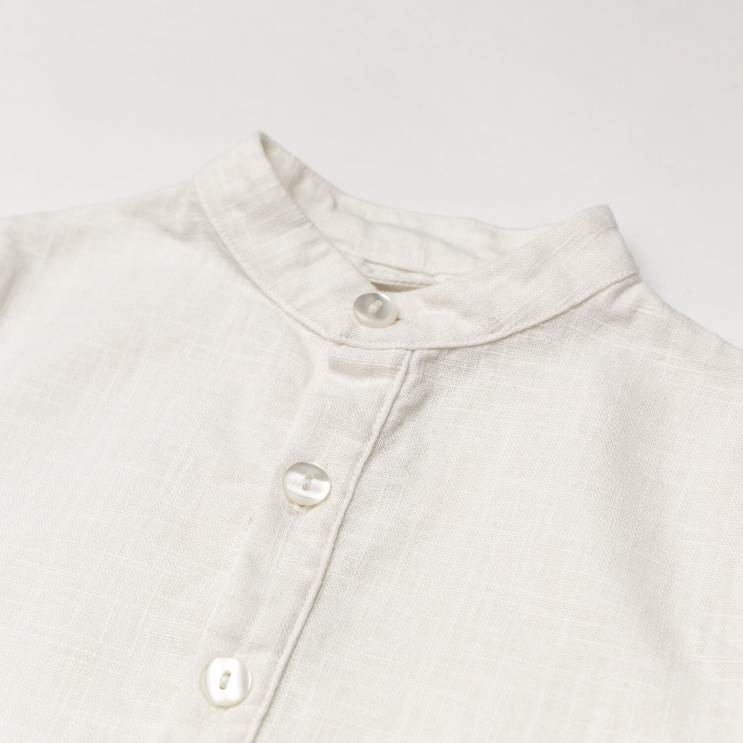 Close-up of the collar and buttons on a white linen short-sleeve shirt for babies and toddlers.