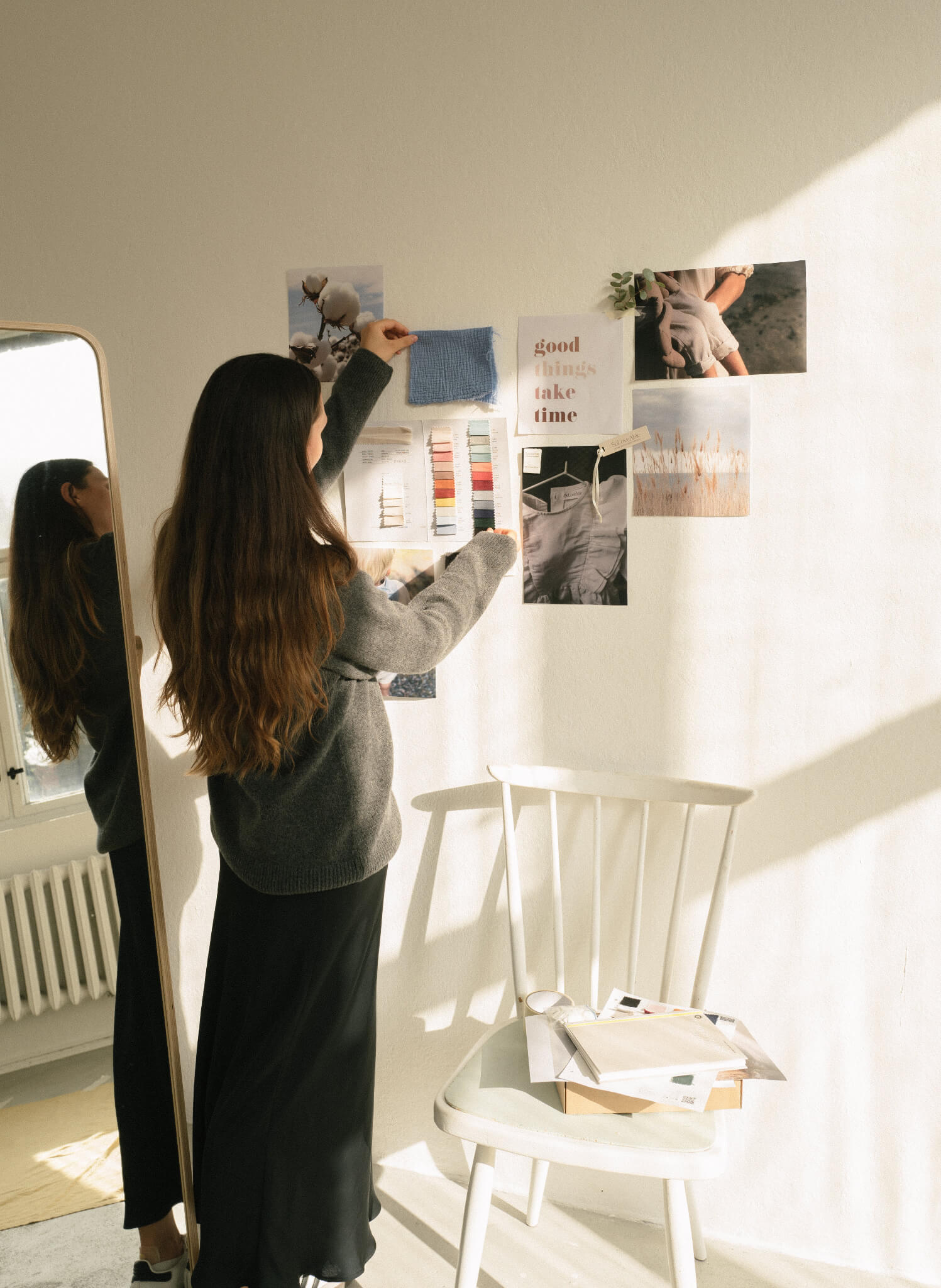 Person arranging fabric samples and moodboard elements in a bright design studio, showcasing sustainable fashion inspiration.