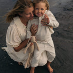 Toddler in beige linen pants and matching linen shirt being held outdoors at the beach.