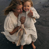 Toddler in beige linen pants and matching linen shirt being held outdoors at the beach.