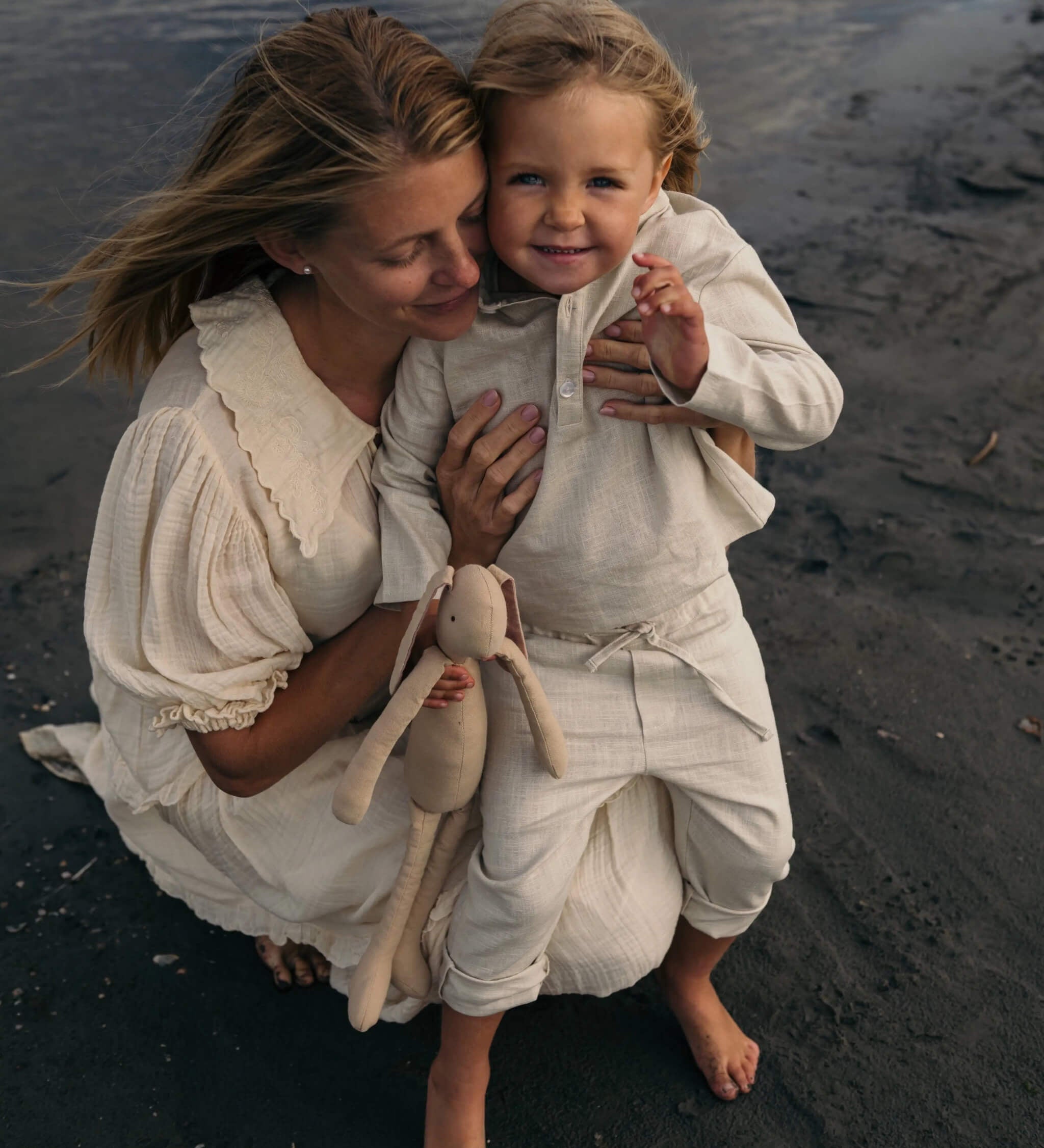 Toddler in beige linen pants and matching linen shirt being held outdoors at the beach.
