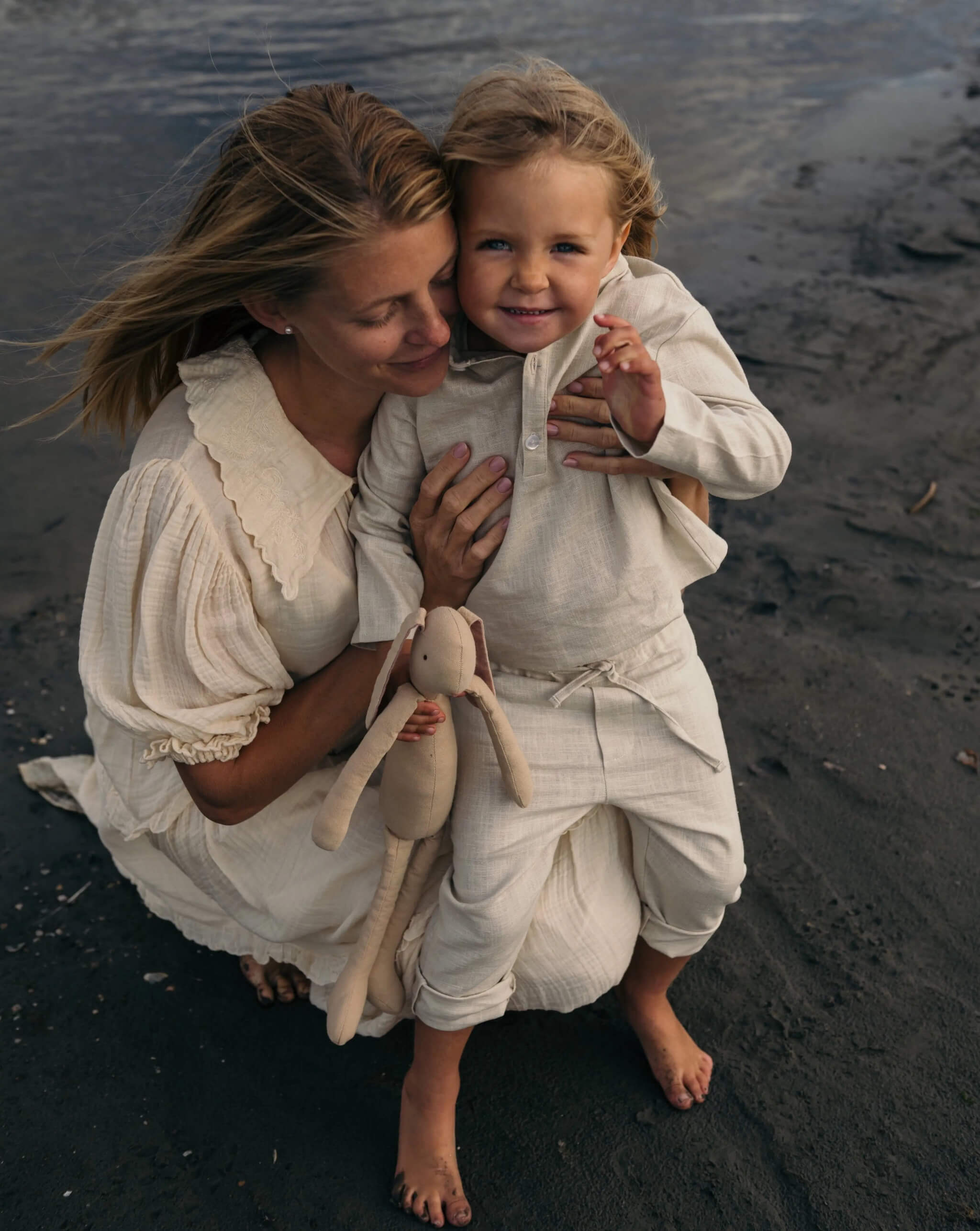 Toddler in beige linen pants and matching linen shirt being held outdoors at the beach.