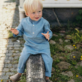 Toddler wearing a light blue linen shirt and matching linen pants sitting outdoors on a stone wall.
