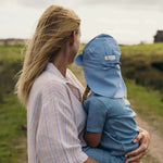 Child wearing blue linen sun hat with neck protection being held outdoors