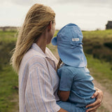 Child wearing blue linen sun hat with neck protection being held outdoors