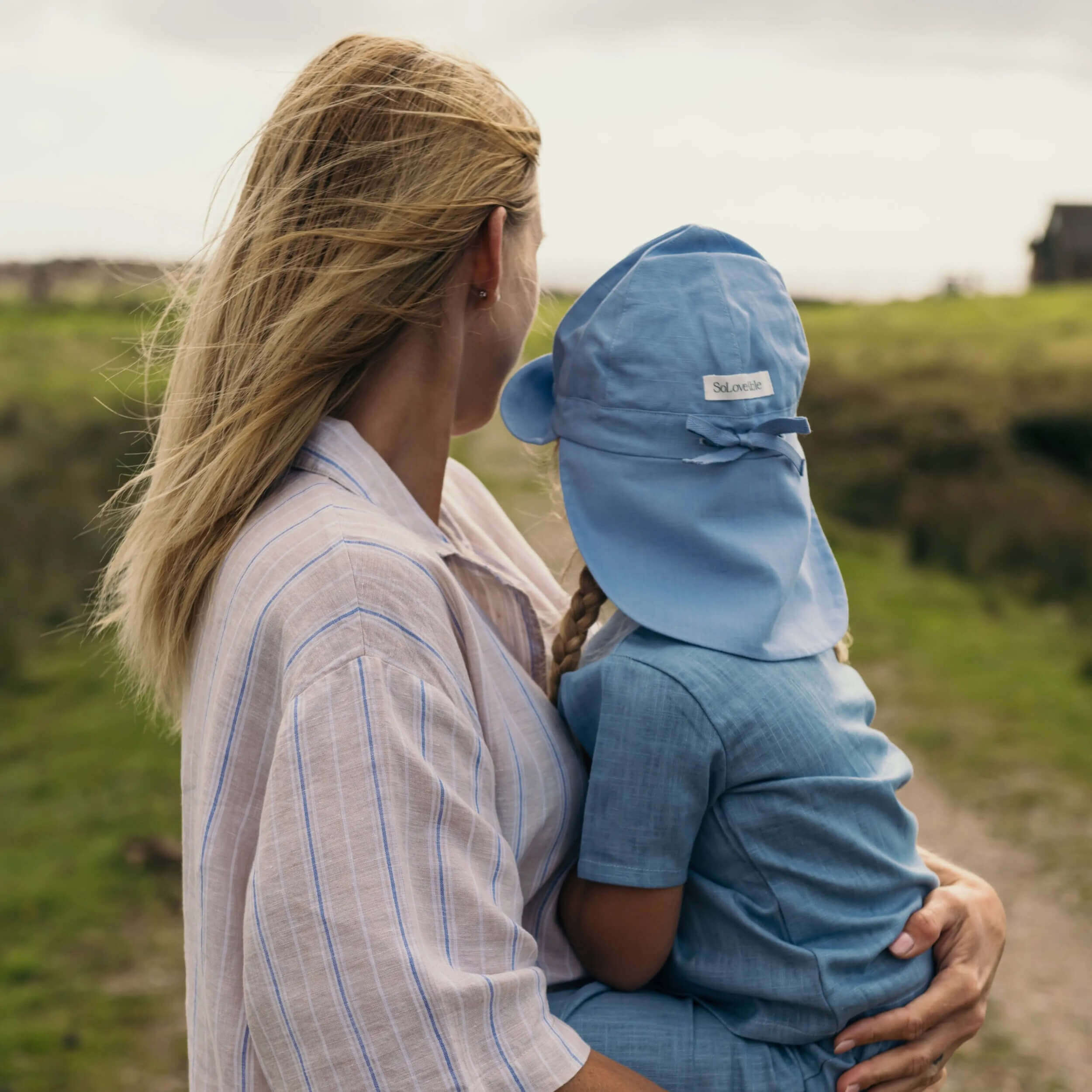 Child wearing blue linen sun hat with neck protection being held outdoors