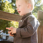 Toddler wearing a long-sleeve brown linen shirt outdoors.
