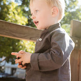 Toddler wearing a long-sleeve brown linen shirt outdoors.