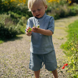 Toddler wearing light blue linen shorts and a matching linen shirt while exploring outdoors on a sunny day.