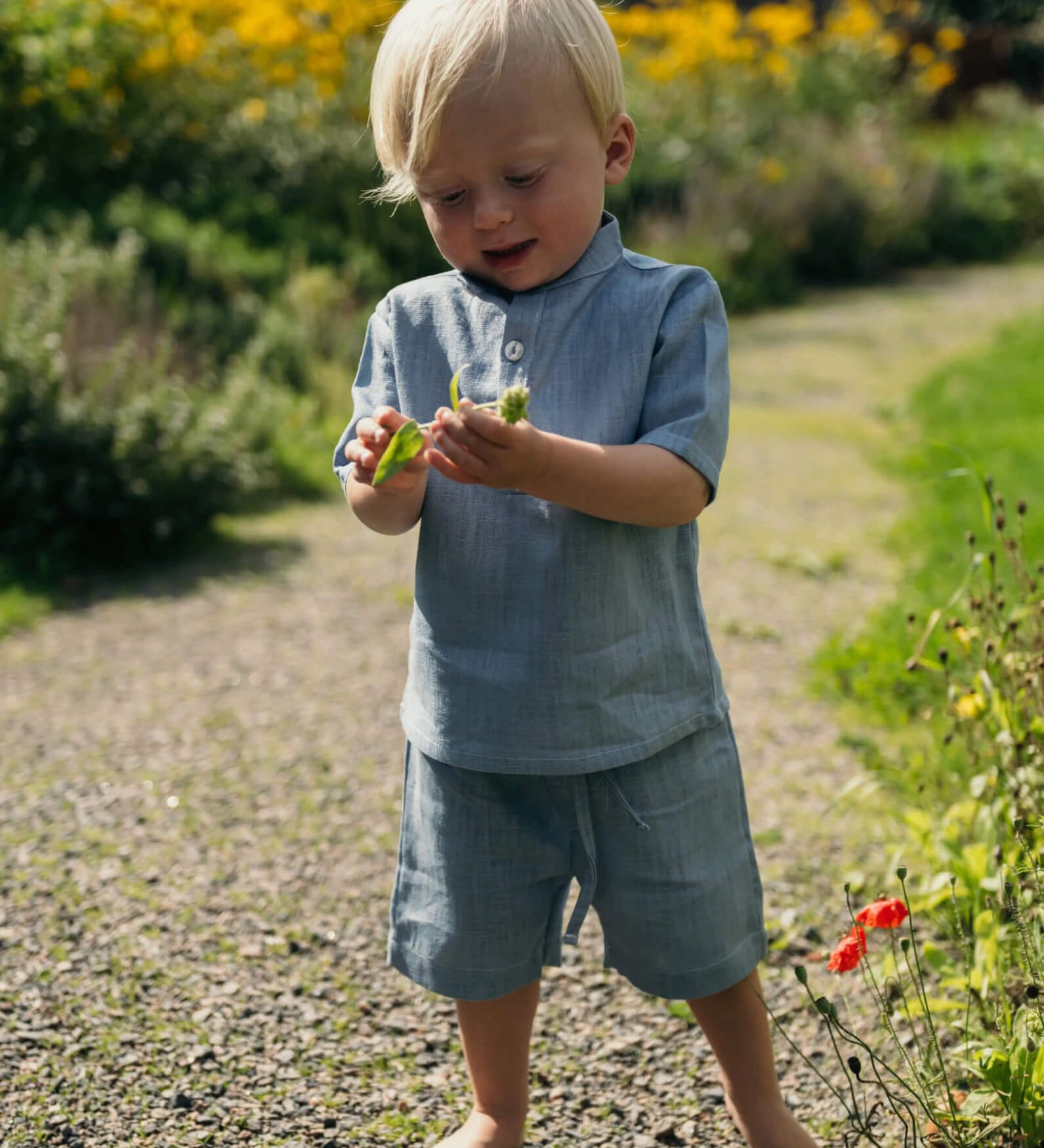 Toddler wearing light blue linen shorts and a matching linen shirt while exploring outdoors on a sunny day.