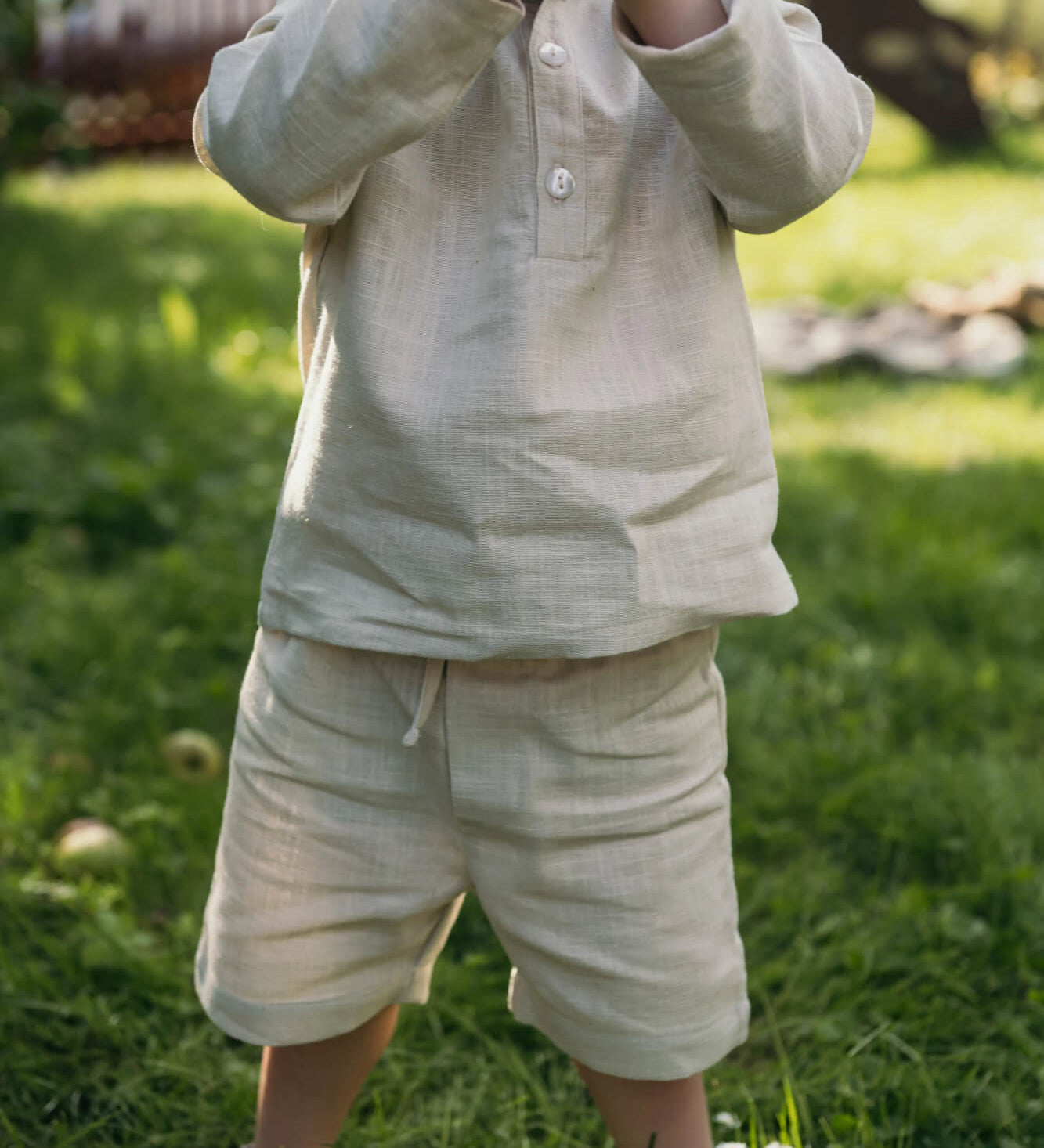 Toddler wearing short beige linen pants and a matching linen shirt outdoors on a sunny day.
