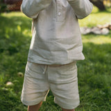 Toddler wearing short beige linen pants and a matching linen shirt outdoors on a sunny day.