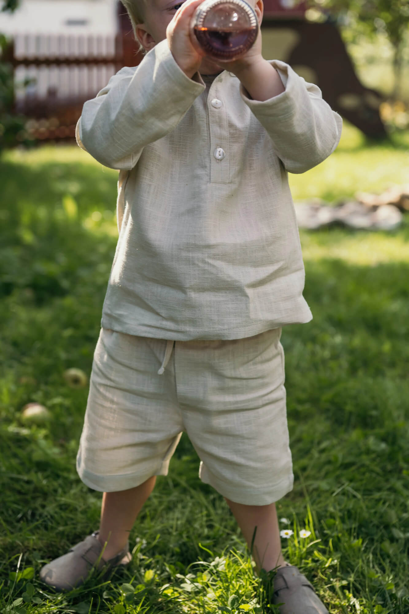 Toddler wearing short beige linen pants and a matching linen shirt outdoors on a sunny day.