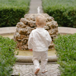 Toddler wearing soft white linen pants and matching top, photographed from the back.
