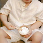 Toddler wearing a white linen short-sleeve shirt eating ice cream outdoors.