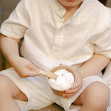 Toddler wearing a white linen short-sleeve shirt eating ice cream outdoors.