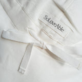 Close-up of white linen baby sun hat with SoLoveAble logo and adjustable tie detail
