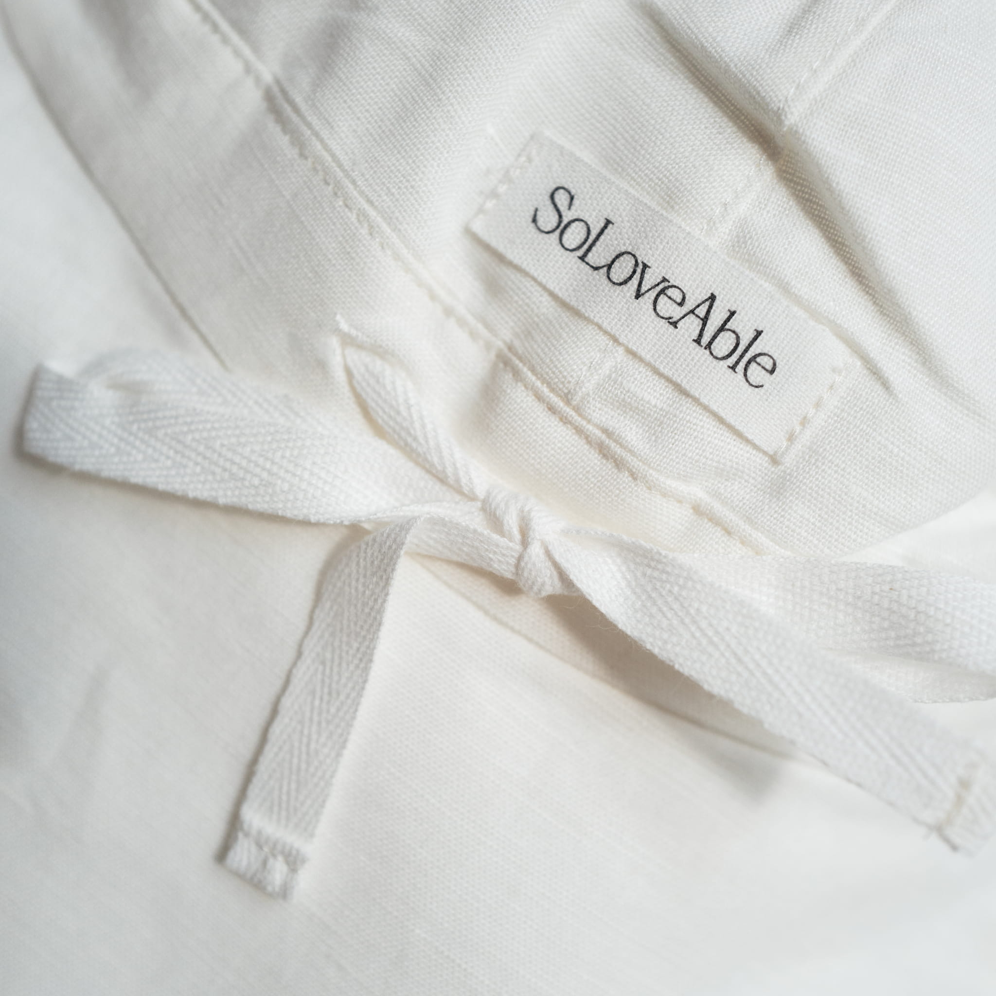 Close-up of white linen baby sun hat with SoLoveAble logo and adjustable tie detail