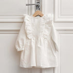 White linen kids dress with ruffle details hanging on a wooden hanger in a bright room