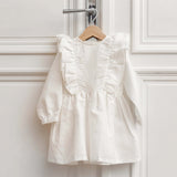 White linen kids dress with ruffle details hanging on a wooden hanger in a bright room